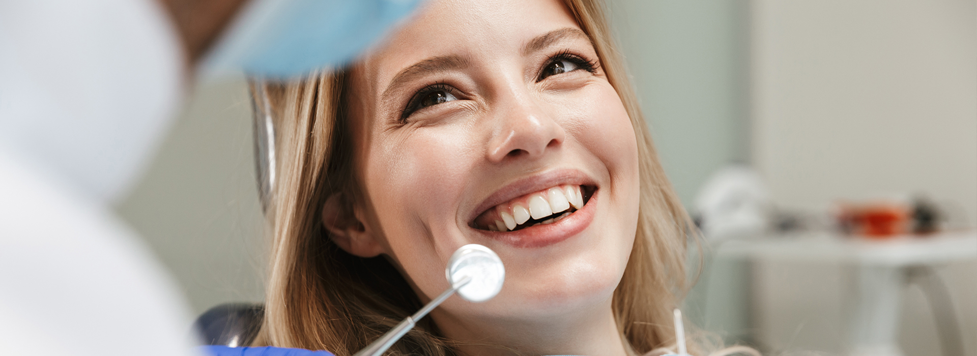Woman sitting in dental chair with smiling expression, looking towards camera.