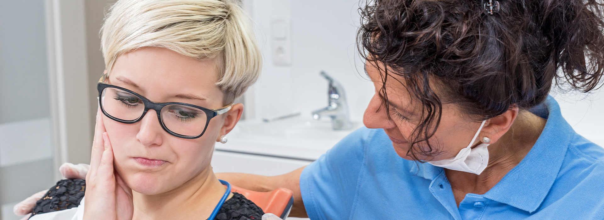 A woman receiving dental care from a professional, with both individuals wearing face masks.