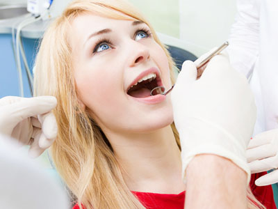 A woman sitting in a dentist's chair with her mouth open, receiving dental care from a professional holding tools.
